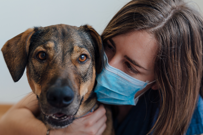 mulher com máscara de proteção contra coronavírus abraçando cachorro